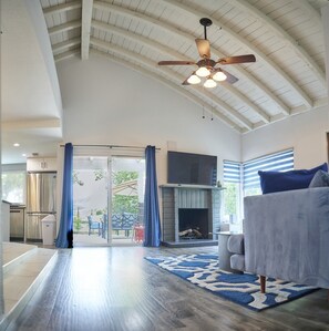 A spacious living area with a fireplace, a ceiling fan, and a large TV. - LA DOLCE VITA (Palm Springs)