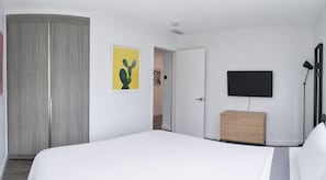 Quarto com cama, guarda-roupa, televisão e porta que dá para outro cômodo.