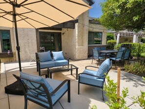 Un espace extérieur aménagé en terrasse, avec des coins salon comprenant des canapés et des fauteuils, le tout abrité sous un grand parasol.