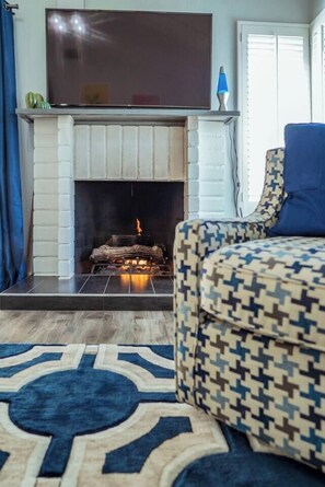Una sala de estar con chimenea, un sofá estampado y una alfombra azul.