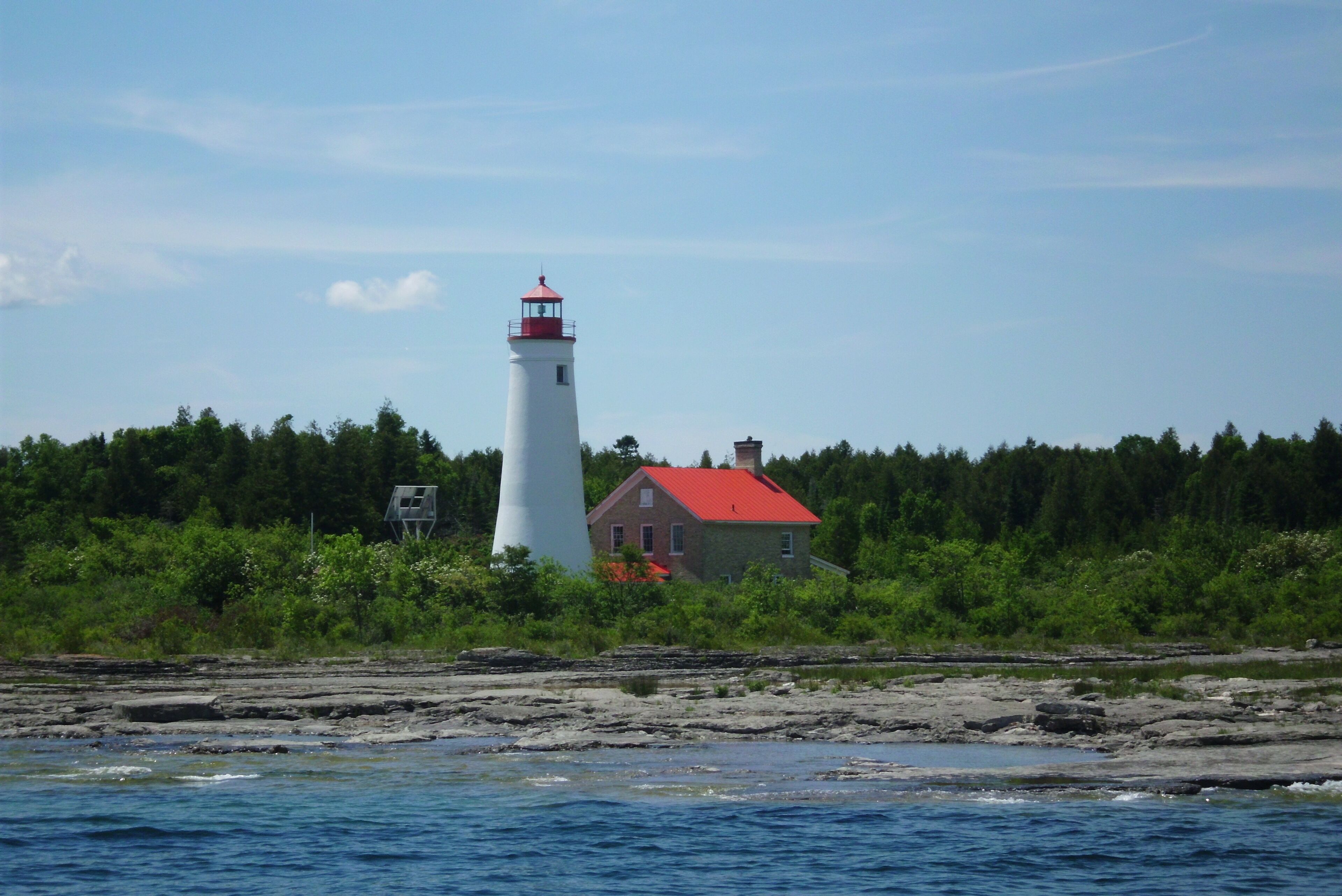 A lighthouse with a red roof and a white tower, situated on a rocky shoreline with a red-roofed building nearby.
