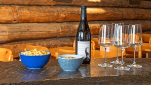 A rustic wooden table with a bottle of wine, two bowls of snacks, and three wine glasses.