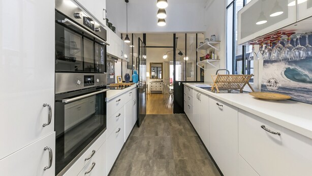 Una cocina moderna con electrodomésticos de acero inoxidable, muebles blancos e iluminación colgante.