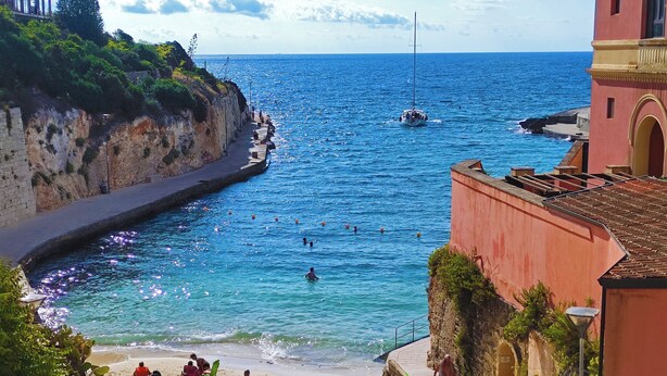 Un paysage côtier avec une plage, un bateau sur l’eau et un bâtiment à la façade rouge.