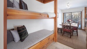 A bunk bed with a grey mattress and pillows, wooden beams, and a view of a dining area with a table and chairs. - RMR: Chokeberry 3813 Condo in The Aspens (Wilson)