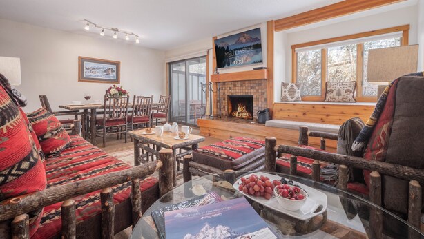 A cozy living room with a fireplace, wooden furniture, and a large window. - RMR: Chokeberry 3813 Condo in The Aspens (Wilson)