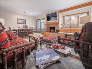 A cozy living room with a fireplace, wooden furniture, and a large window. - RMR: Chokeberry 3813 Condo in The Aspens (Wilson)