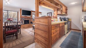 A spacious kitchen with wooden cabinetry, a dining area with a fireplace, and a large window offering a view of trees. - RMR: Chokeberry 3813 Condo in The Aspens (Wilson)