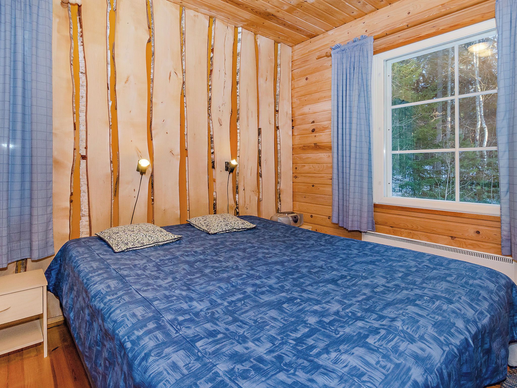 Quarto de cabana de madeira com cama, duas almofadas, janela e radiador.