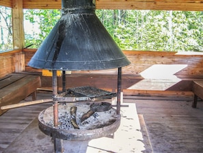Una estufa de leña con chimenea, rejilla metálica y fuego encendido en su interior.