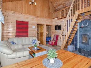 A wooden interior with a sofa, a table with a plant, a fireplace, and a staircase.