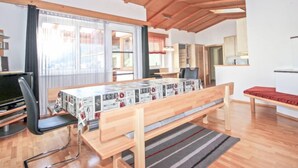 A room with a wooden ceiling, a large window with curtains, a dining table with a patterned tablecloth, a black office chair, and a bed with a red blanket. - Vacation home Dialer by Interhome (Umhausen)