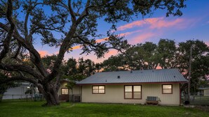 A single-story house with a sloped roof, a front porch, and a large tree in the foreground. - Ranch Style House 1/2 Block from Fulton Park & Fishing Pier on Aransas Bay. (Fulton)