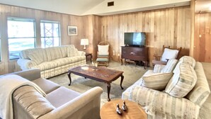 A living room with a sofa, armchair, wooden coffee table, and a television on a wooden cabinet. - Ranch Style House 1/2 Block from Fulton Park & Fishing Pier on Aransas Bay. (Fulton)