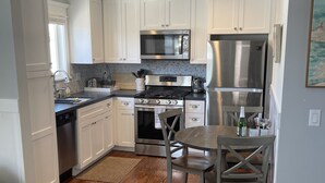 A modern kitchen with white cabinets, stainless steel appliances, and a wooden floor.