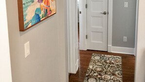 A hallway with a wooden floor, a white door, and a colorful painting on the wall.