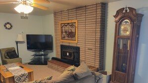 A living room with a fireplace, a television, a sofa, a lamp, and a clock.