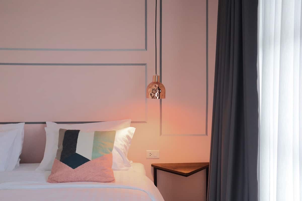Una cama bien hecha con varias almohadas, una mesita de noche y una lámpara fijada a la pared.
