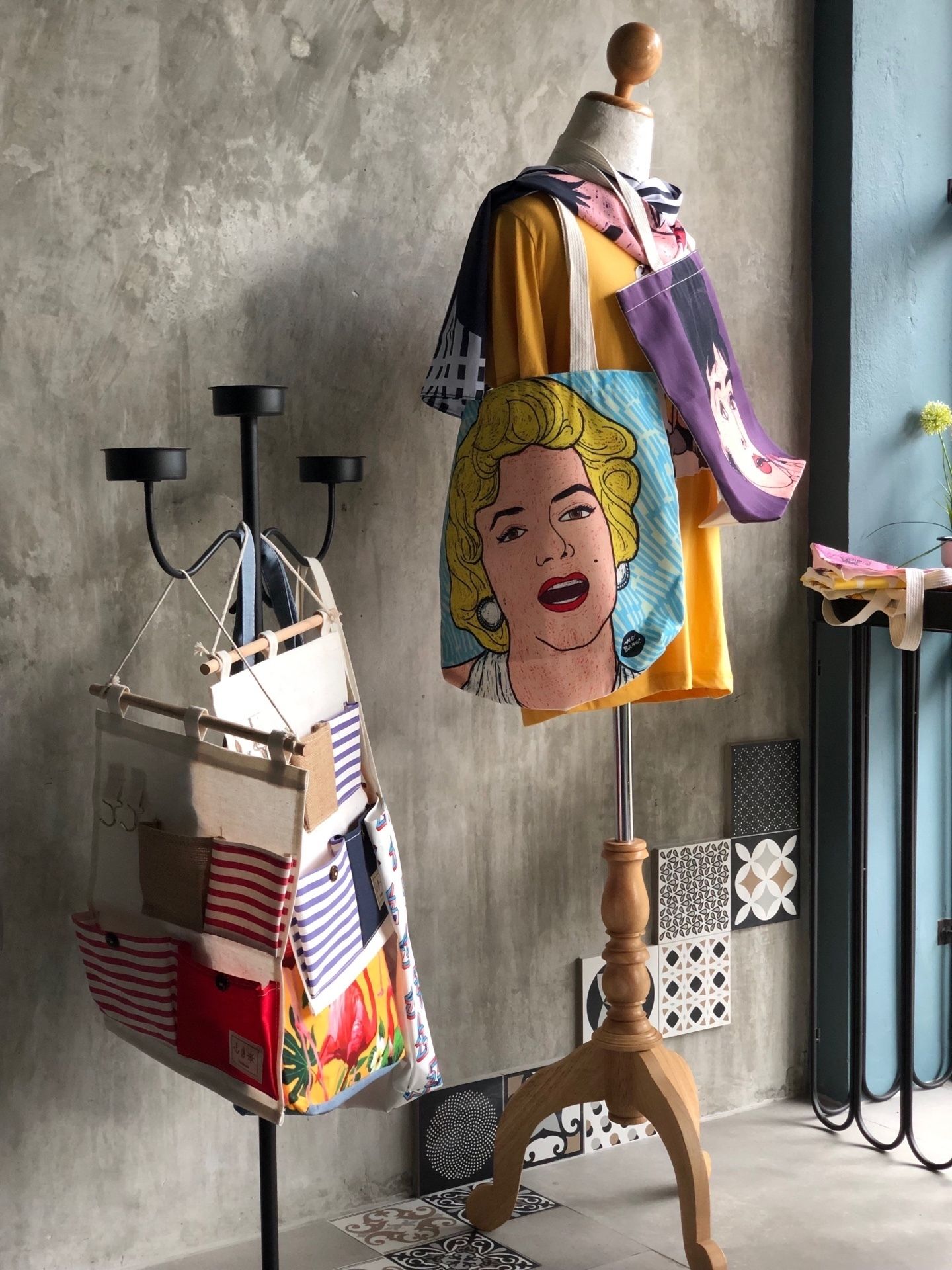 A mannequin with a colorful jacket, a rack of striped bags, and patterned tiles on the floor.
