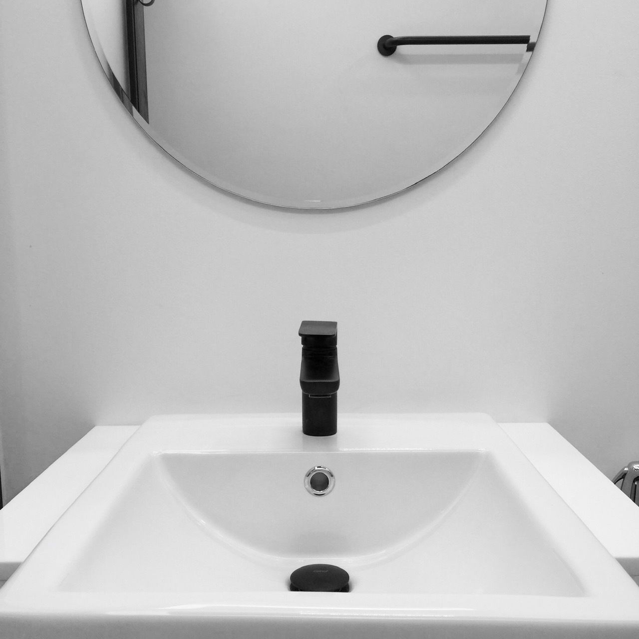 A white bathroom sink with a black faucet, a round mirror above it, and a towel rack to the right.