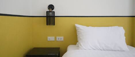 A hotel room with a bed, a nightstand, and a wall-mounted lamp.