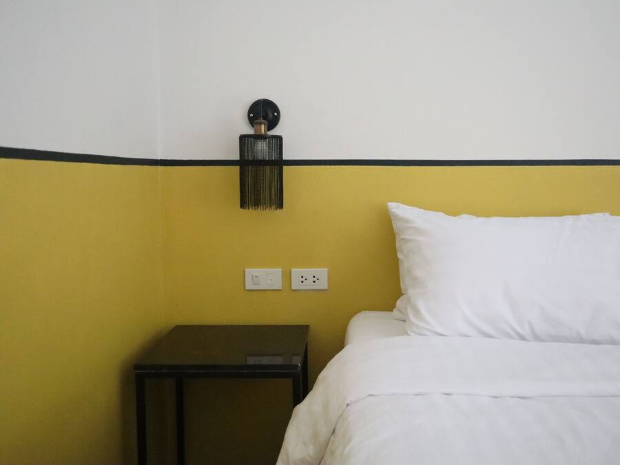 Et hotelværelse med en seng, et natbord og en lampe på væggen.