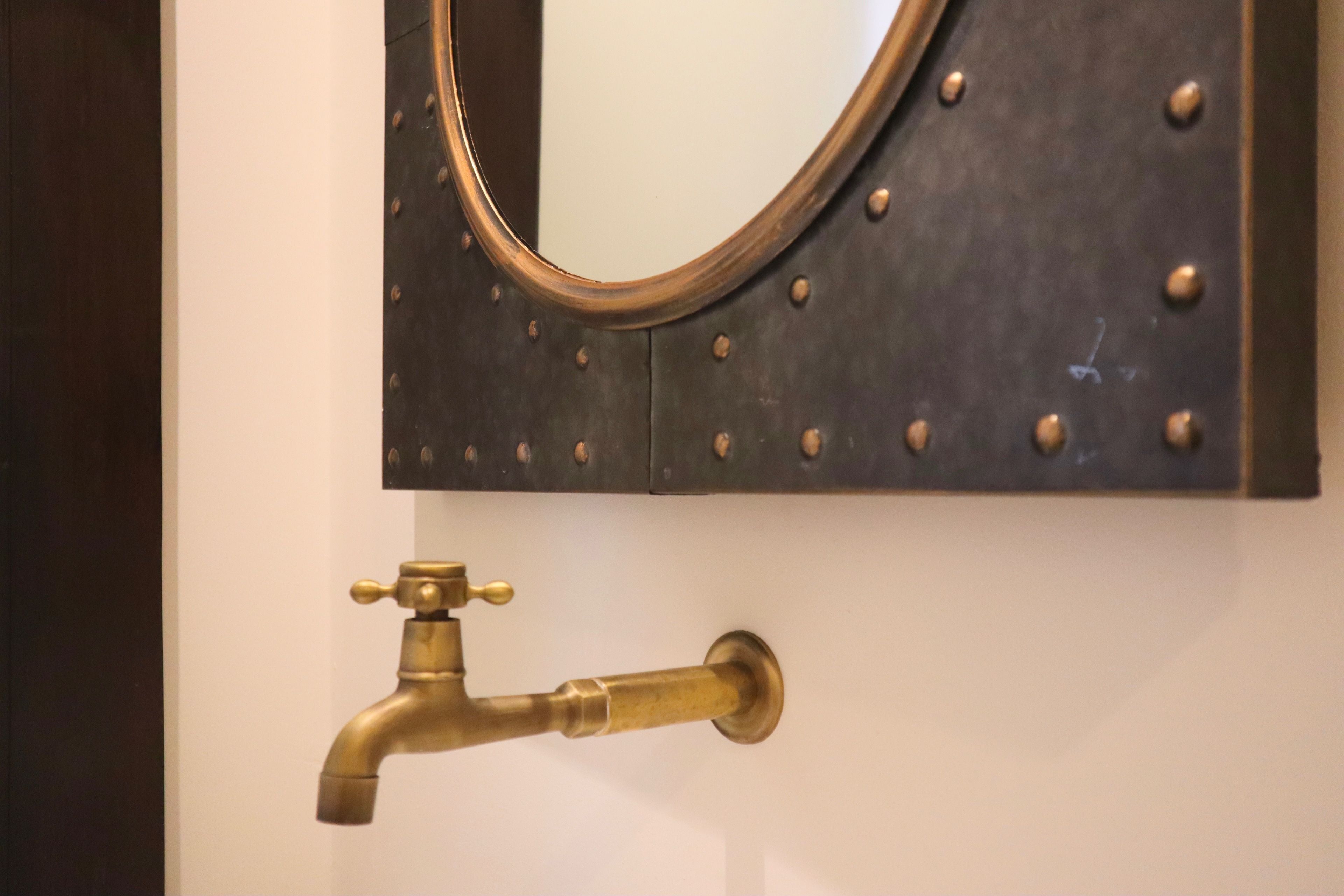 A wall-mounted mirror with a circular frame and a brass faucet below it.