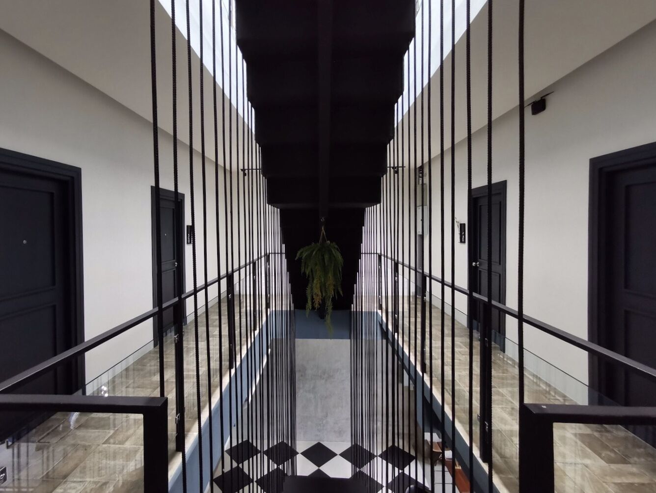 A modern hallway with black railings, a hanging plant, and a patterned floor.