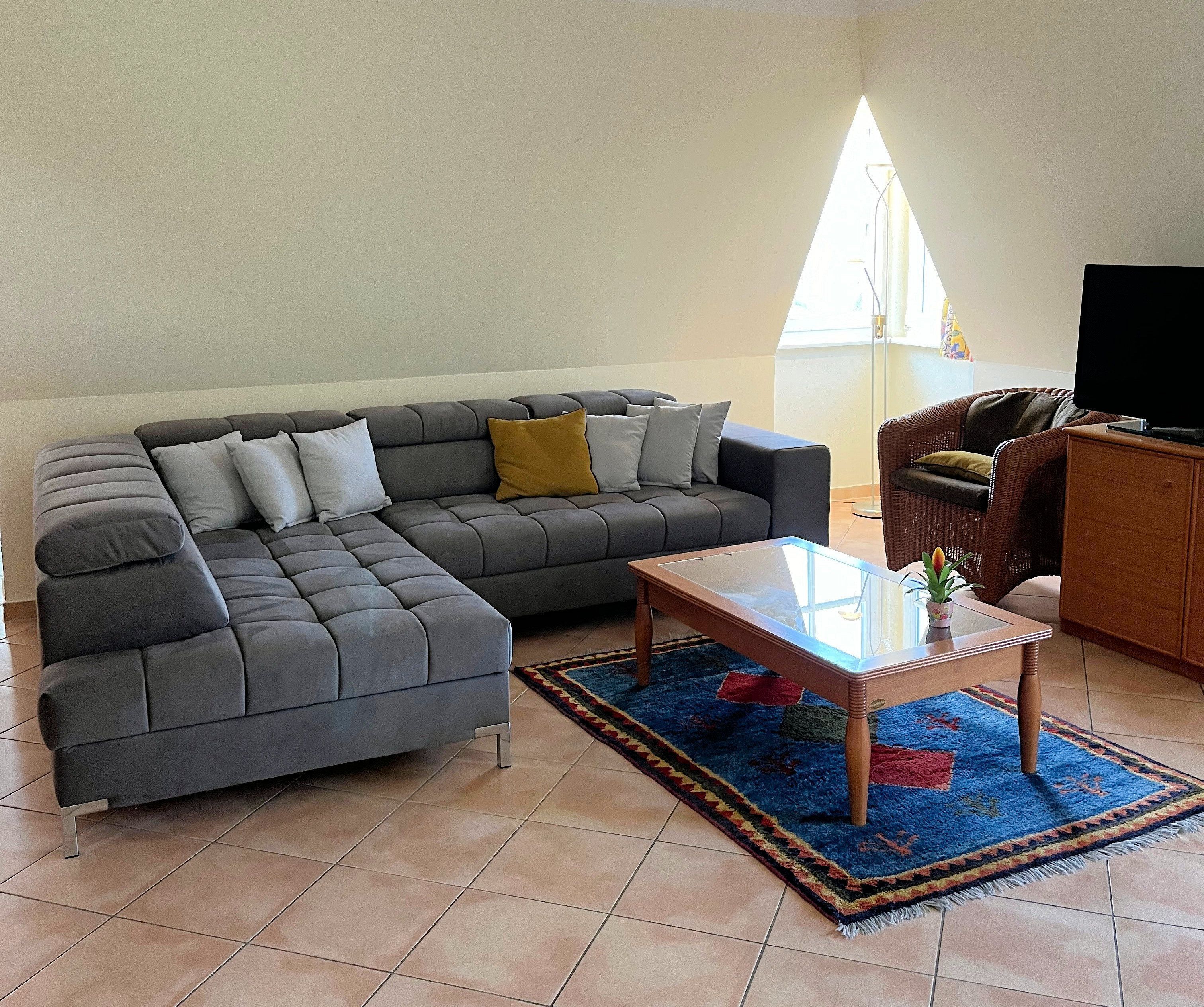 A living room with a sectional sofa, a coffee table, a wicker chair, and a television.