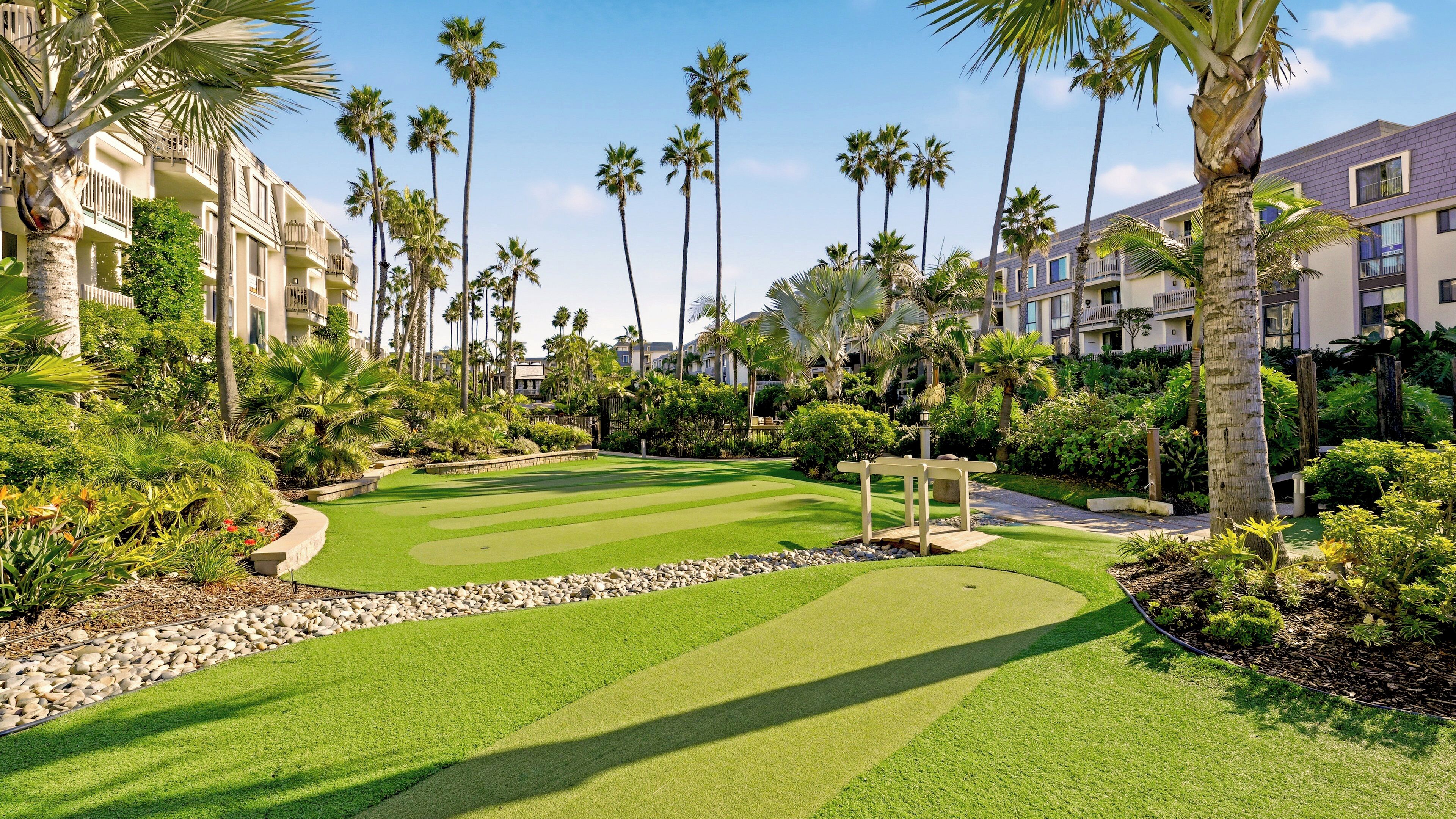 A golf course with palm trees and a well-maintained lawn, surrounded by buildings with balconies.