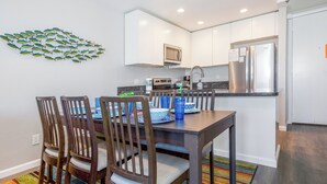Una cocina moderna con armarios blancos, un refrigerador de acero inoxidable y un comedor con sillas de madera y un tapete colorido.
