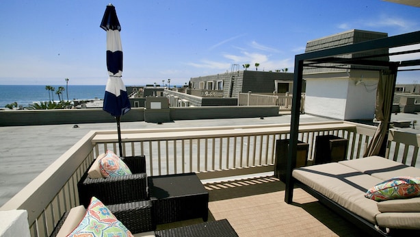 A rooftop terrace with outdoor seating, a view of the ocean, and a modern building in the background. - B306 - Luxury Penthouse with spacious deck. Enjoy ocean View from Deck lounge sun bed (Oceanside)