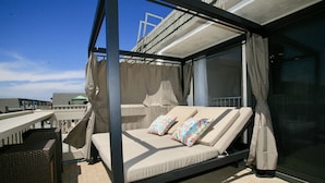A balcony with a bed, two colorful pillows, and a view of the cityscape. - B306 - Luxury Penthouse with spacious deck. Enjoy ocean View from Deck lounge sun bed (Oceanside)