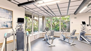 Un gimnasio con equipo de ejercicio, ventanas amplias y techo con vigas a la vista.