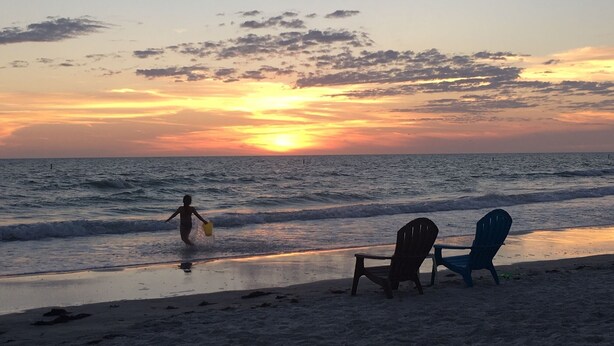A beach scene with a sunset, waves, and two chairs on the sand. - A Perfect Condo Near The Beach - just renovated! (St Pete Beach)