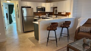 A modern kitchen with white cabinets, stainless steel appliances, and a central island with bar stools. - A Perfect Condo Near The Beach - just renovated! (St Pete Beach)