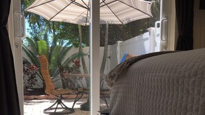 A bedroom with a bed, a glass door leading to a patio with a table, chairs, and plants. - A Perfect Condo Near The Beach - just renovated! (St Pete Beach)