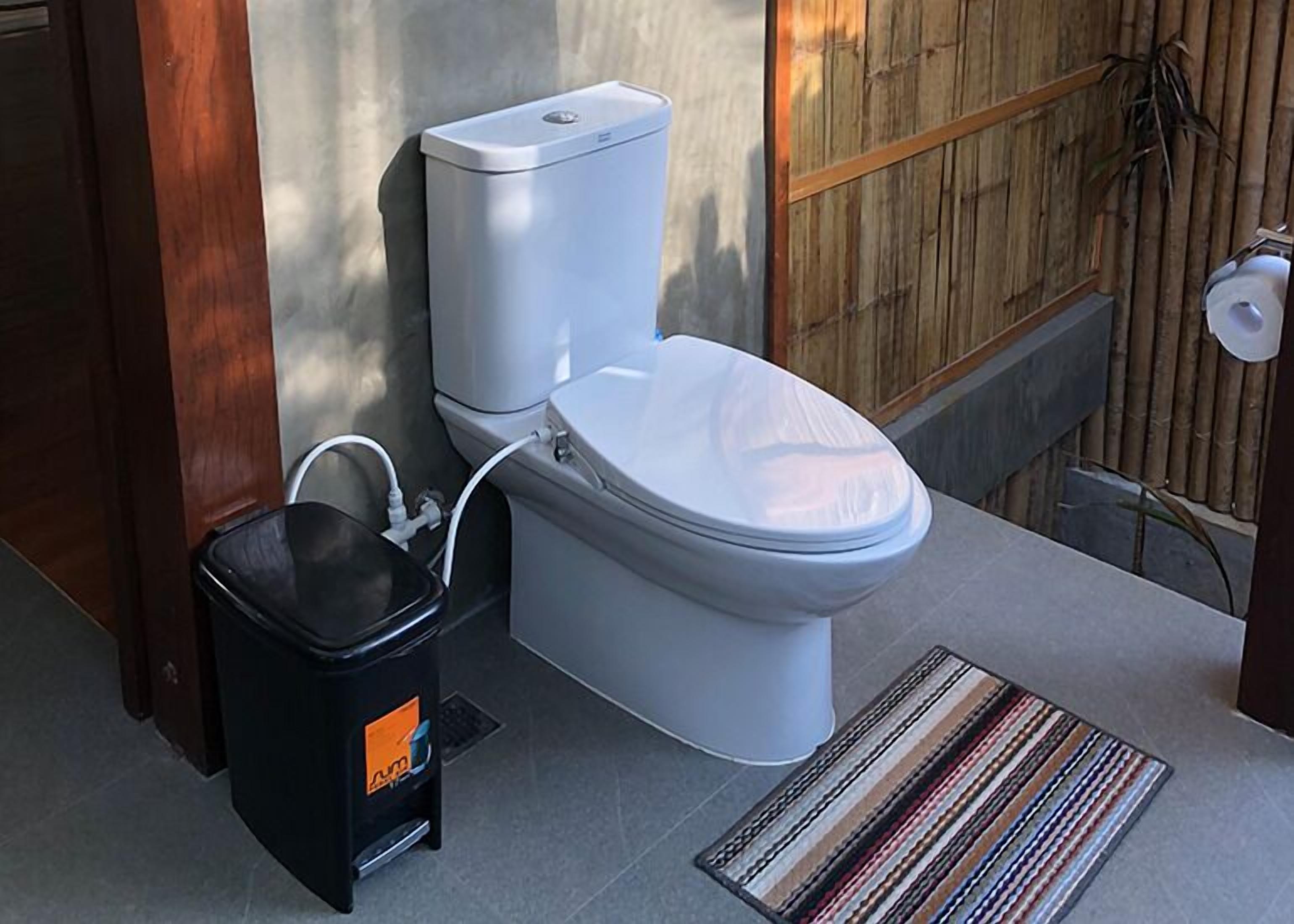 A modern bathroom with a white toilet, a black bidet, and a striped rug on the floor.