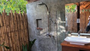 A modern bathroom with a glass shower enclosure, a wooden vanity, and a bamboo fence. - Sadhana Siargao (General Luna)