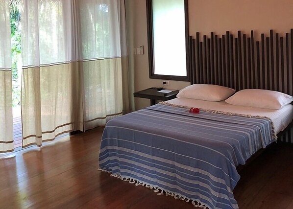 A bedroom with a bed, a nightstand, a window with curtains, and a wall with vertical slats.