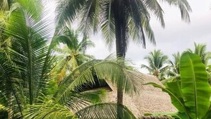 A tropical setting with a thatched-roof structure surrounded by lush greenery and palm trees. - Sadhana Siargao (General Luna)