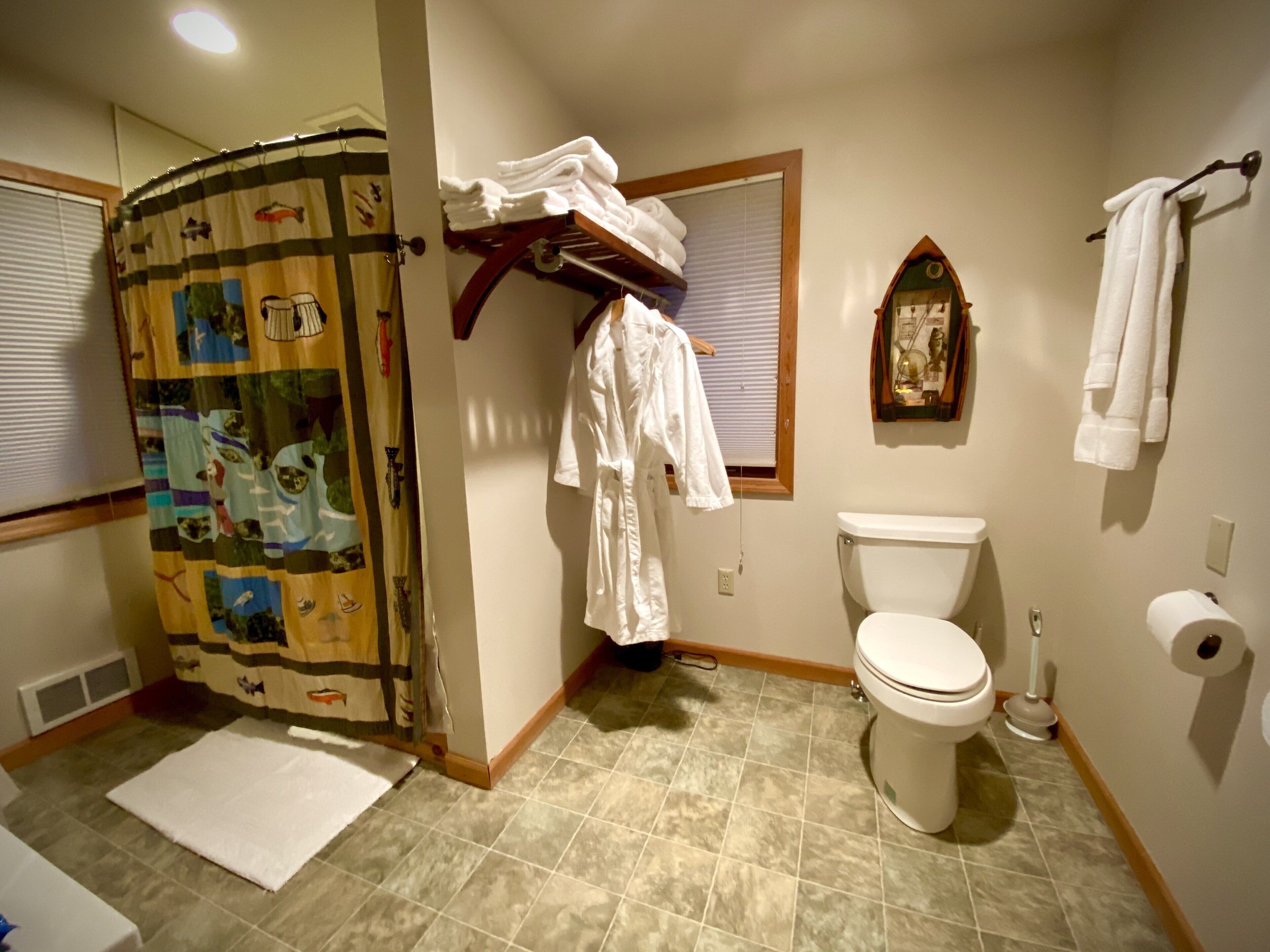 A bathroom with a toilet, a shower curtain, a towel rack, and a window with blinds.