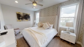 A bedroom with a tufted headboard, a large window with curtains, a ceiling fan, and a bedside table with a lamp. - Encore Resort at Reunion 1865 (Kissimmee)
