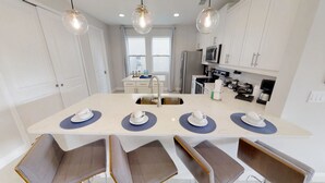 Une cuisine moderne dotée d’un îlot central, de meubles blancs et d’un coin repas avec quatre chaises.