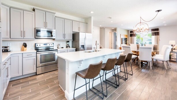 A modern kitchen with stainless steel appliances, a large island with bar stools, and a dining area with a chandelier. - Encore Resort at Reunion 1855 (Kissimmee)