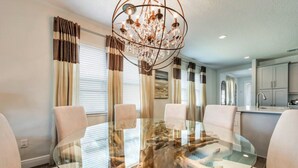 A modern dining area with a glass table surrounded by chairs, a chandelier, and a view of the kitchen. - Encore Resort at Reunion 1855 (Kissimmee)