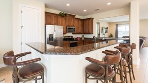 A modern kitchen with granite countertops, stainless steel appliances, and a central island with bar stools. - Encore Resort at Reunion 1866 (Kissimmee)