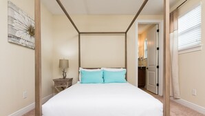 A four-poster bed with white bedding and two teal pillows, a bedside table with a lamp, and a wall-mounted artwork. - Encore Resort at Reunion 1866 (Kissimmee)