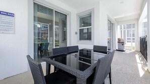 A glass-top table with wicker chairs, a pool rules sign, and a grill outside. - Champions Gate 1564 (Davenport)