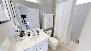 A modern bathroom with a white sink, toilet, and shower curtain. A tripod is visible in the background, suggesting a photo opportunity. - Golden Palms Vacation Resort 1847 (Kissimmee)
